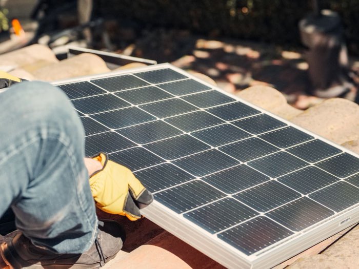 Beispielfoto: Handwerker legt ein Solarmodul auf einem Ziegeldach zurecht.